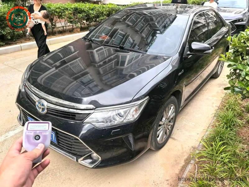 Black earlier Toyota Camry Hybrid in a front three-quarter view with a paint gauge in the foreground